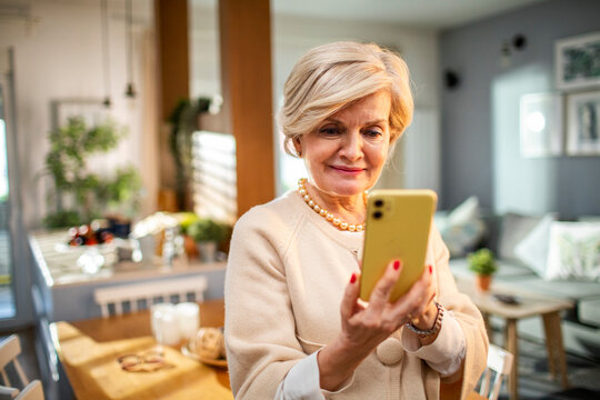 Elderly senior woman holding smartphone standing at home