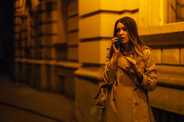Woman walking in a dark city streets and using a mobile phone