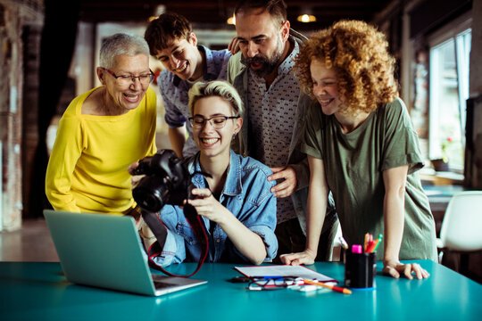 Female photographer holding dslr camera looking at picture with colleagues in office