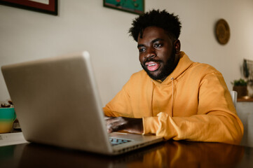 A cheerful interracial young casual entrepreneur is working on a laptop from home.