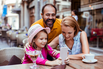 Little girl holding cell phone with parents in outdoor cafe