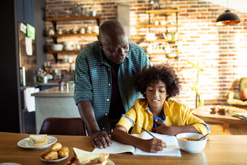 Happy African American father and son sitting at table doing homework together at home