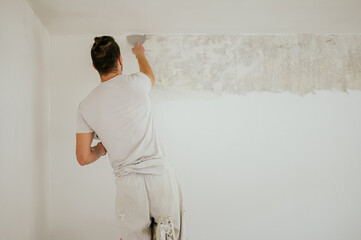 Rear view of a builder skim coating walls with plaster.