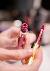 Lipstick: the artist's brush is a bright red color, and it is surrounded by a variety of other makeup brushes and products.