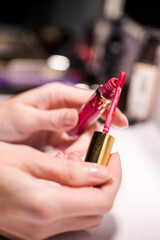 Lipstick: the artist's brush is a bright red color, and it is surrounded by a variety of other makeup brushes and products.