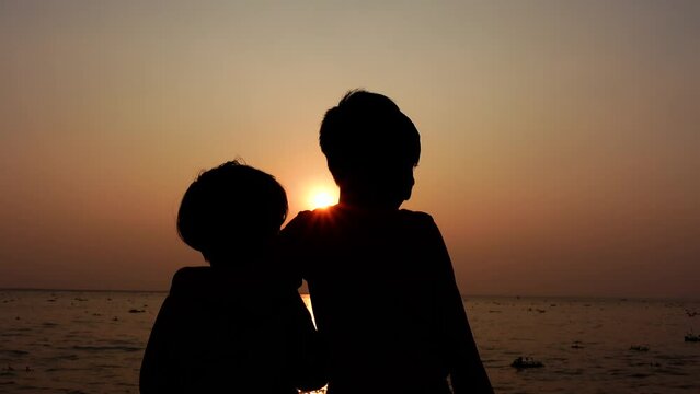 Two children are standing on the river bank at sunset enjoying the evening river view. Silhouette views two kids having fun in the evening time. Two Brothers in Holiday conceptual 4k video.
