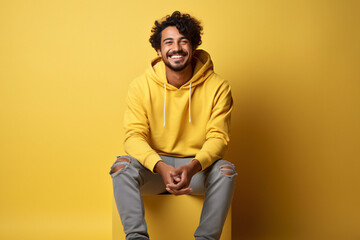 portrait of a man. Young smiling happy Indian man wears t-shirt casual clothes, sits with mobile cell phone, yellow background. studio portrait