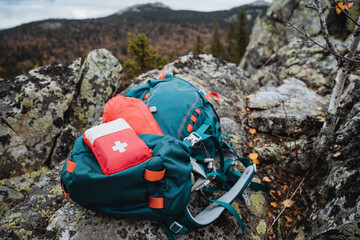 A red hiking first aid kit is on a backpack in the mountains, tourist equipment.