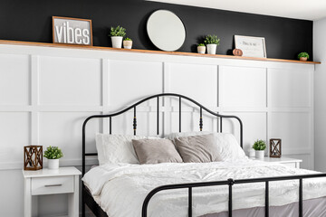 A farmhouse bedroom detail shot with wainscoting, decorations on a natural wood shelf with black paint above, and a black metal bed frame.	