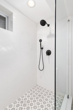 A bathroom shower with herringbone and mosaic tiles, a black showerhead, and a glass shower wall.