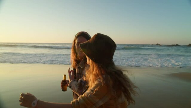 Two female friends walk on beach at sunset. California surfing lifestyle vibes. Cinematic evening light at sunset on pristine beach. Millennial women hang out. Friendship concept. Surfcamp location