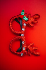 Christmas masquerade glasses with deer antlers on a red background. The concept of a Christmas party. A fun holiday. Decoration for children and adults.
