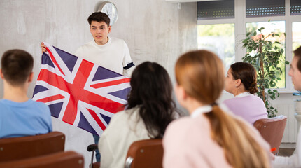 Young lecturer demonstrating flag of Great Britain to group of interested adult students sitting on...