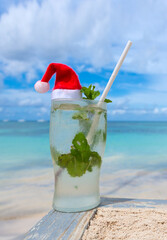 Christmas background with drinks Bocal with Santa hat on Caribbean beach.