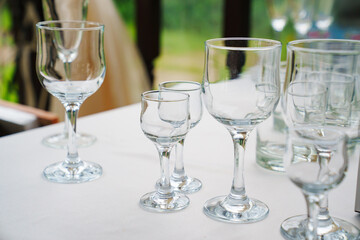 Empty wine glasses and shot glasses on a table with a white tablecloth.