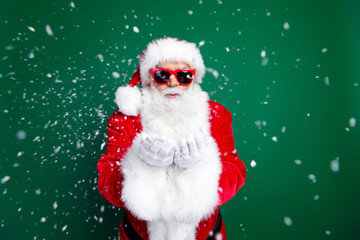 Photo portrait of elderly retired man blowing snow hands wear trendy santa claus costume coat isolated on green color background