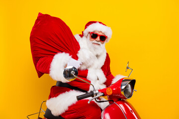 Profile portrait of cheerful santa drive bike carry christmas presents bag isolated on yellow color background
