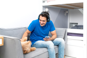 Positive guy sits on the couch and plays with his cute dog