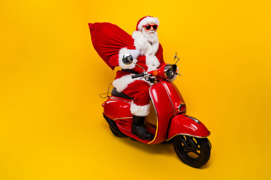 Side photo of grey white hair beard cool santa claus ride drive scooter xmas night deliver present sack isolated on yellow color background