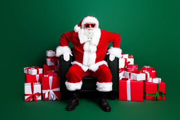Full length photo of funny good mood claus wear red costume preparing christmas presents sitting armchair isolated green color background
