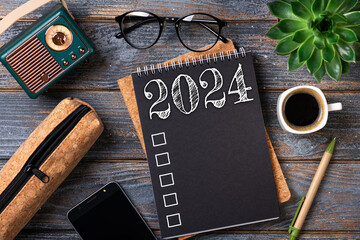 New year resolutions 2024 on desk. 2024 goals list with notebook, coffee cup, plant on wooden table. Resolutions, plan, goals, action, checklist, idea concept. New Year 2024 resolutions. Copy space - obrazy, fototapety, plakaty