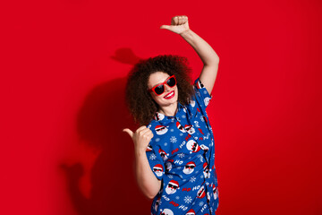 Photo portrait of pretty young girl fingers point empty space dressed stylish blue x-mas print outfit isolated on red color background