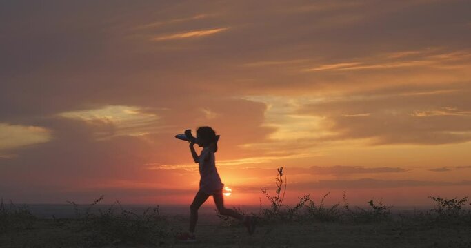 Excited kid runs and jumps with toy airplane against sunset. Happy childhood, family holiday, kid dream. Happy kid at sunset. Silhouette shot