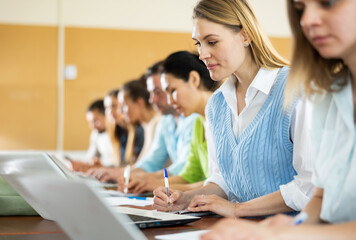 Obraz premium Portrait of concentrated womens and mens studying in classroom, listening to teacher and writing in notebook