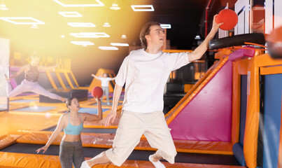 Active guy teenager in sportswear plays ball in trampoline center..