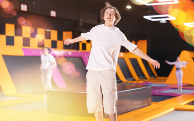 Active guy teenager trains jumping on trampoline in trampoline center