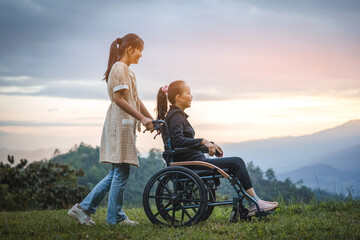 Happy young mother in wheelchair with daughter in spring nature at sunset.