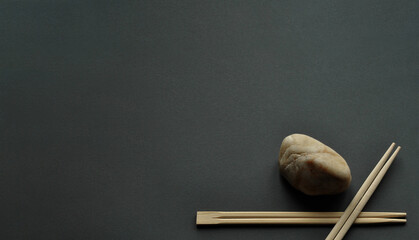 Japanese bamboo chopsticks and light stone on dark gray background. Minimalism, one corner...