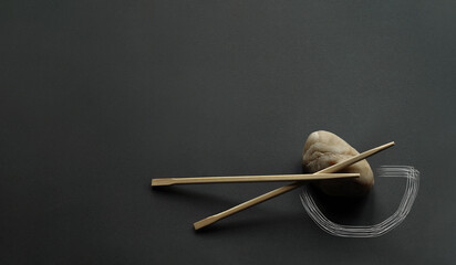 Japanese bamboo chopsticks and light stone on dark gray background. Photo manipulation - delicately drawn bowl silhouette. Minimalism, lines, unique design, corner composition, copy space. No people