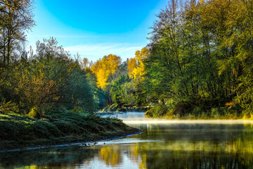 A crisp fall morning on the Sammamish River, with colorful trees and the blue sky reflected in the still water.