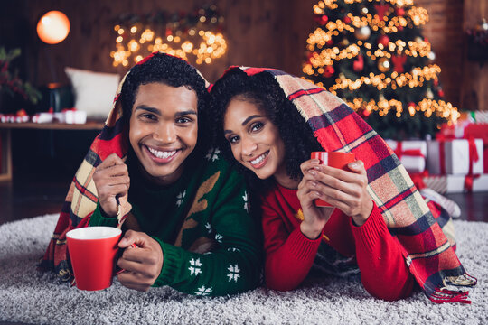Portrait of two idyllic cheerful american people lying blanket covered warm blanket enjoy hot chocolate mug indoors