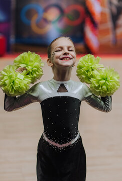 Photo, portrait of a professional sportswoman, a girl cheerleader with green pom-poms in the gym at a cheerleading competition.