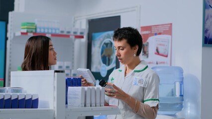 Healthcare expert taking break from arranging merchandise on shelves to help customer with medical...