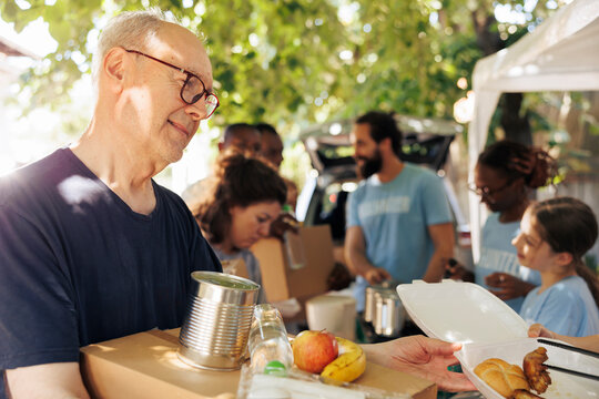 Detailed image of poor, needy caucasian man receiving meal box and canned goods from non-profit food drive. Close-up of low priviliged male individual getting free food from volunteers.