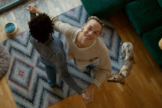 Two happy young multiracial men dancing in living room looking into camera photographed from above