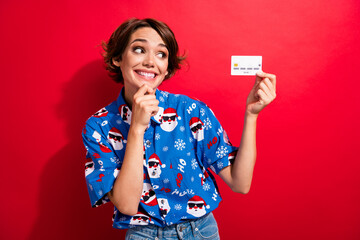 Photo of attractive creative person hand touch chin toothy smile hold debit card isolated on red color background