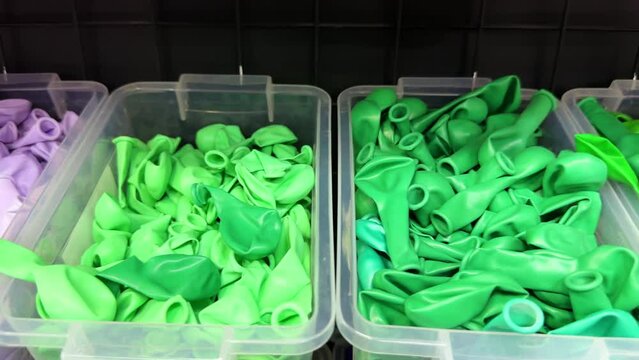 Many colorful balloons deflated in a plastic box on a shelf in a store for holiday events and celebrations. Uninflated balloons in the gift shop.