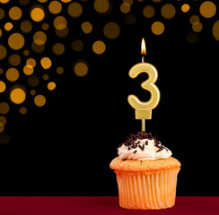 Birthday candle with cupcake - Number 3 on black background with out of focus lights