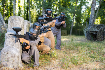 Paintball players of one team in camouflages and masks aiming with gun in shootout outdoors