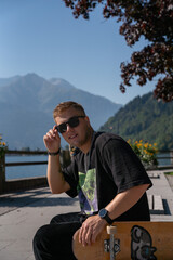 male smiley skateboarder sitting on a park with his longboard or skateboard by his side wearing sunglasses