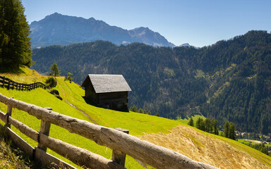Scenic summer mountain landscape with rustic wooden cabins nestled in lush meadow at foot of rocky...