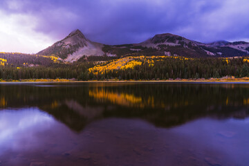 Beautiful purple Sunrise over reflective mirror Lost Lake Colorado in Autumn with yellow Aspen trees and snow covered mountains. 