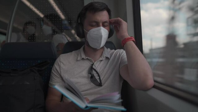 Passenger traveling on Deutsche train in summer with wireless headphones and reading book. Student reads study workbook with wireless earphones while commuting on train. Daily commute to university. 