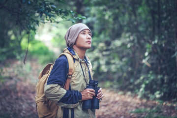 Young man with backpack and holding a binoculars looking in forest wilderness area