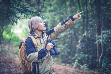 Young man with backpack and holding a binoculars looking in forest wilderness area