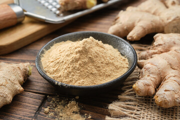 Bowl of ginger ground to powder and whole ginger roots on kitchen table.  A grater with grated ginger root in the background. - obrazy, fototapety, plakaty
